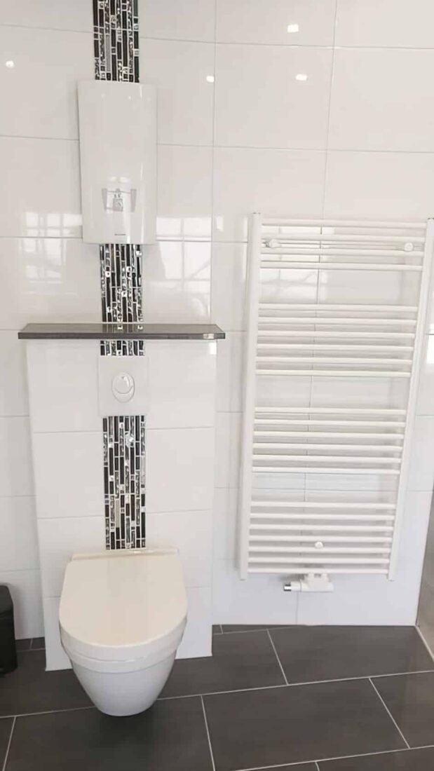 Weißer Durchlauferhitzer an weißer Fliesenwand mit glänzendem Mosaikstreifen
