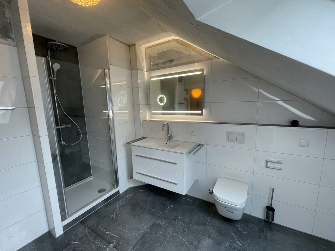 Dachschrägenbad mit Dusche, beleuchtetem Spiegel, Waschtisch und Wand-WC – Badsanierung in Essen