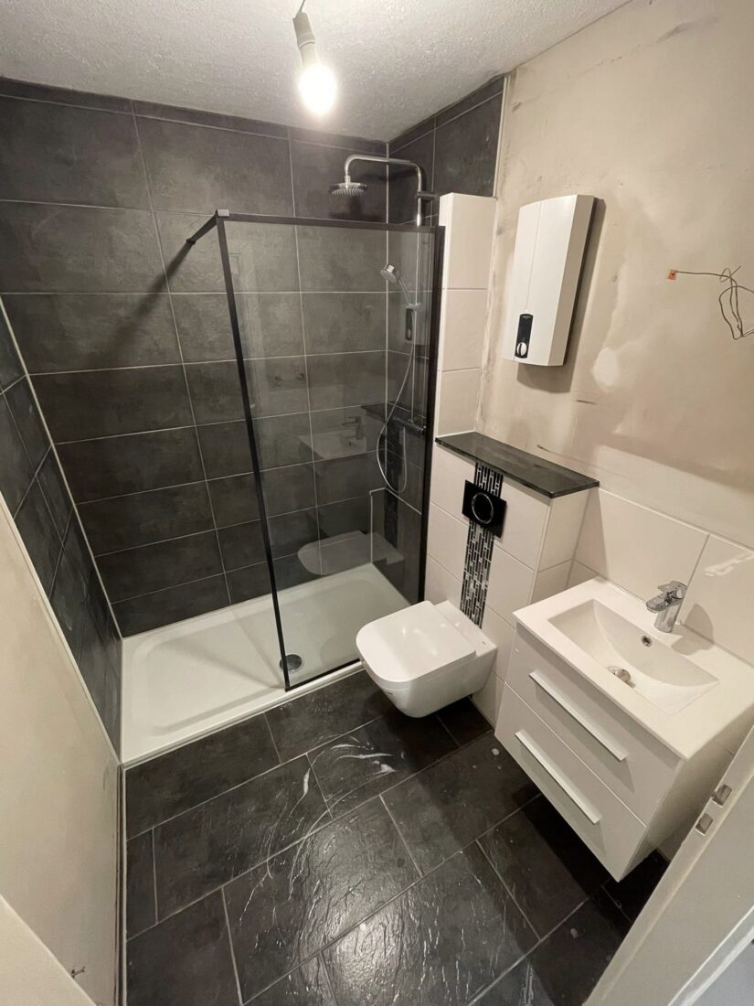 Kleines Bad mit Regendusche, schwarzem Glasprofil, Wand-WC und weißem Waschtisch, anthrazitfarbene Fliesen